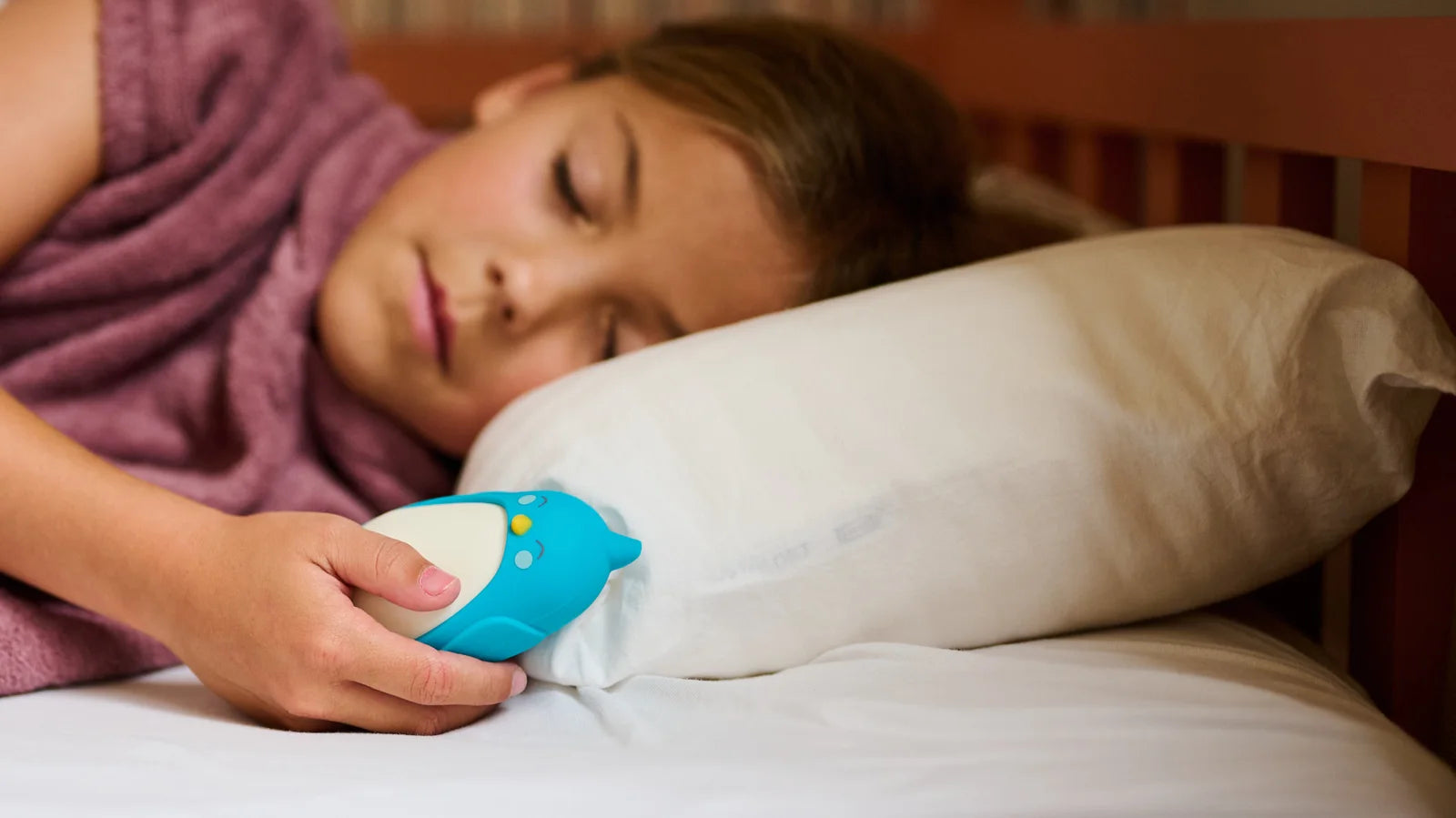 A child asleep in bed holding Bibi the moonbuddy