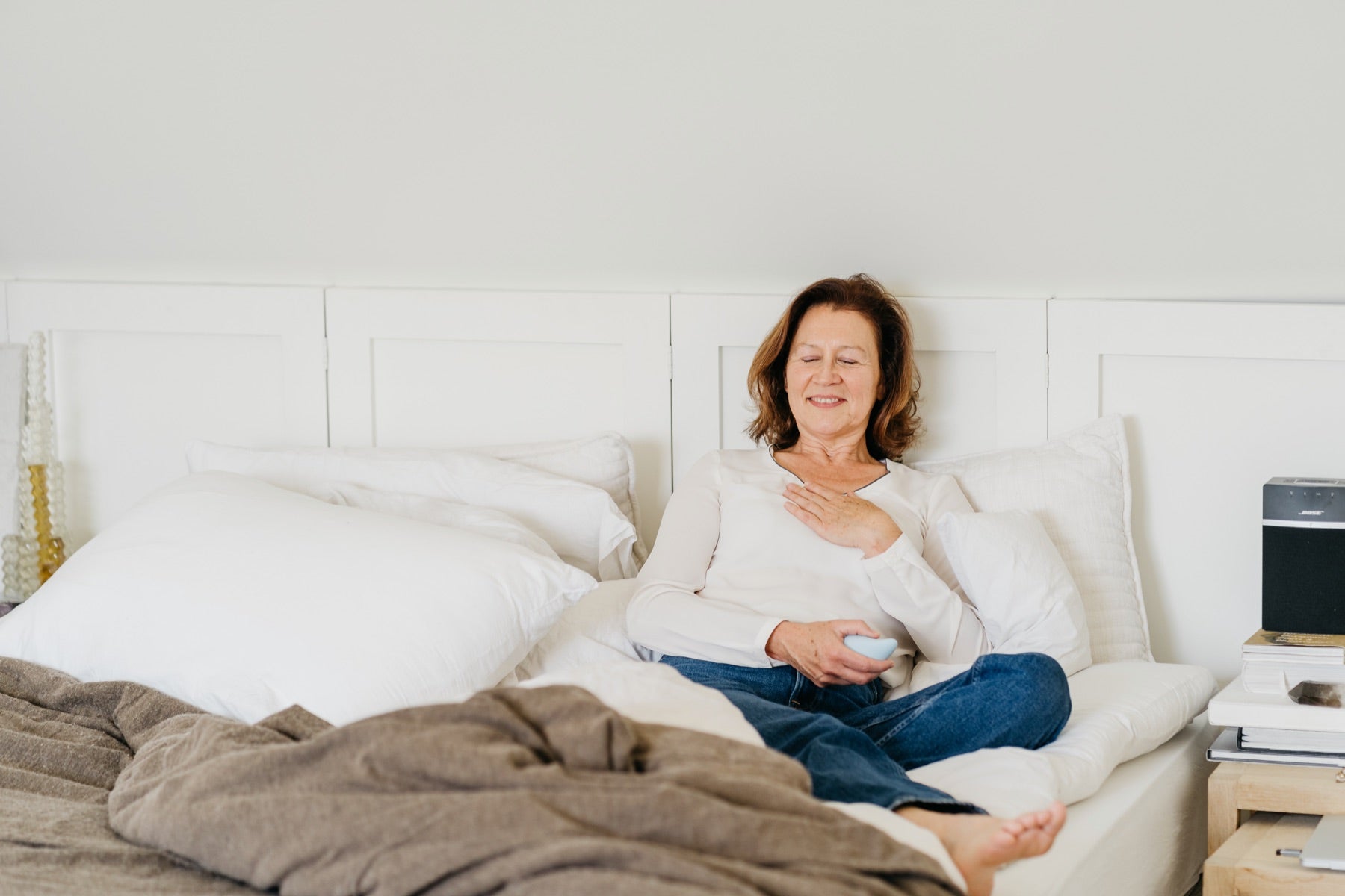 A woman sitting comfortably on a bed, holding moonbird with her eyes closed