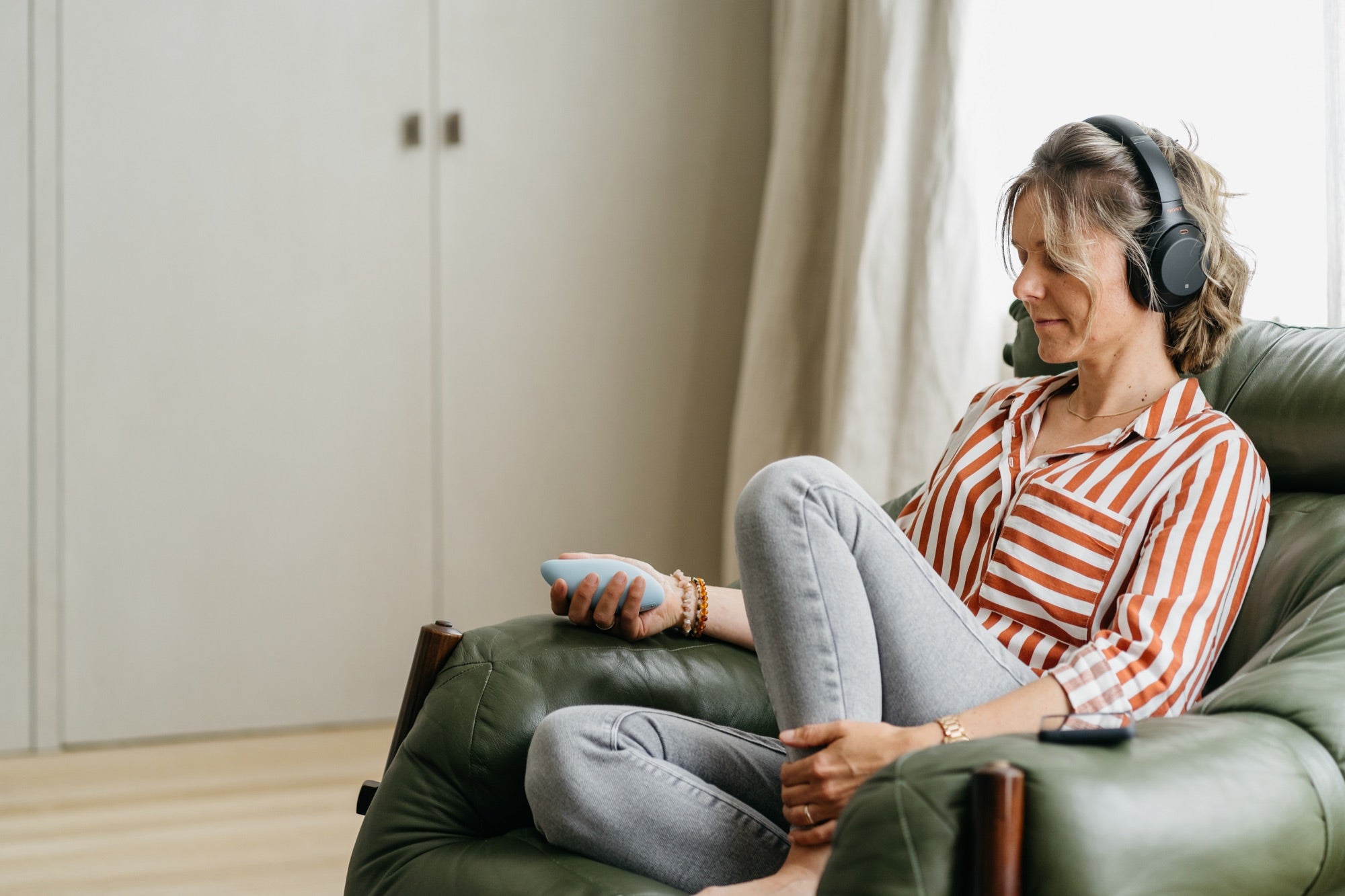 A woman resting in an armchair with headphones on, holding a light blue moonbird
