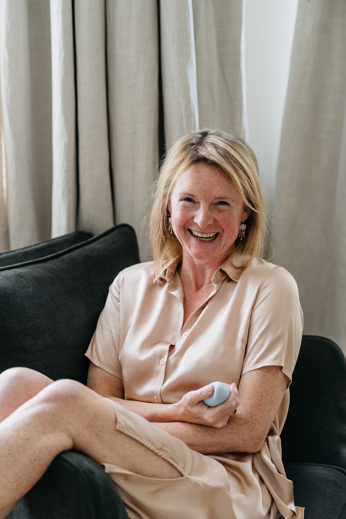 A woman seated on a sofa, smiling while holding a light blue moonbird