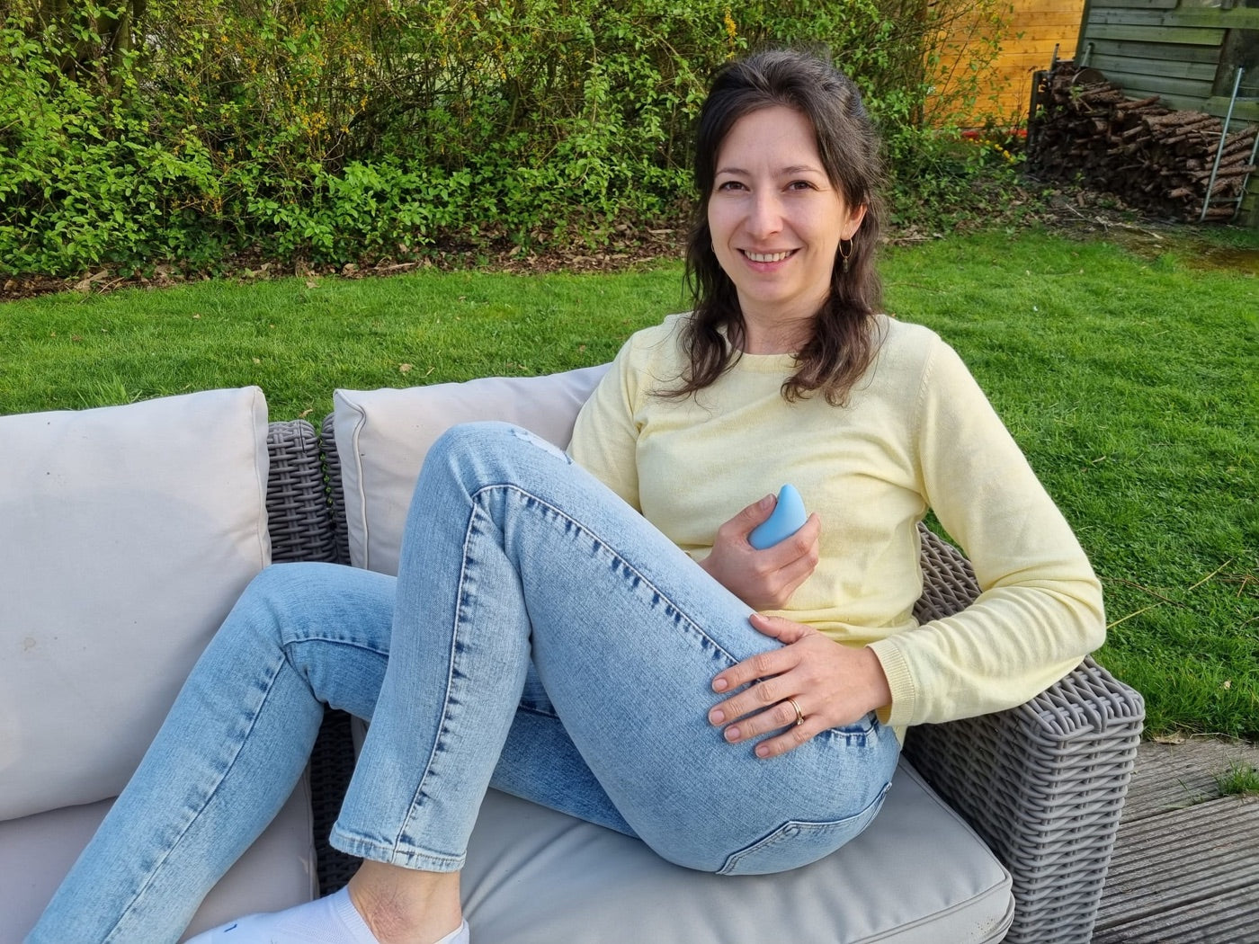 A woman seated on a garden sofa holding a blue moonbird
