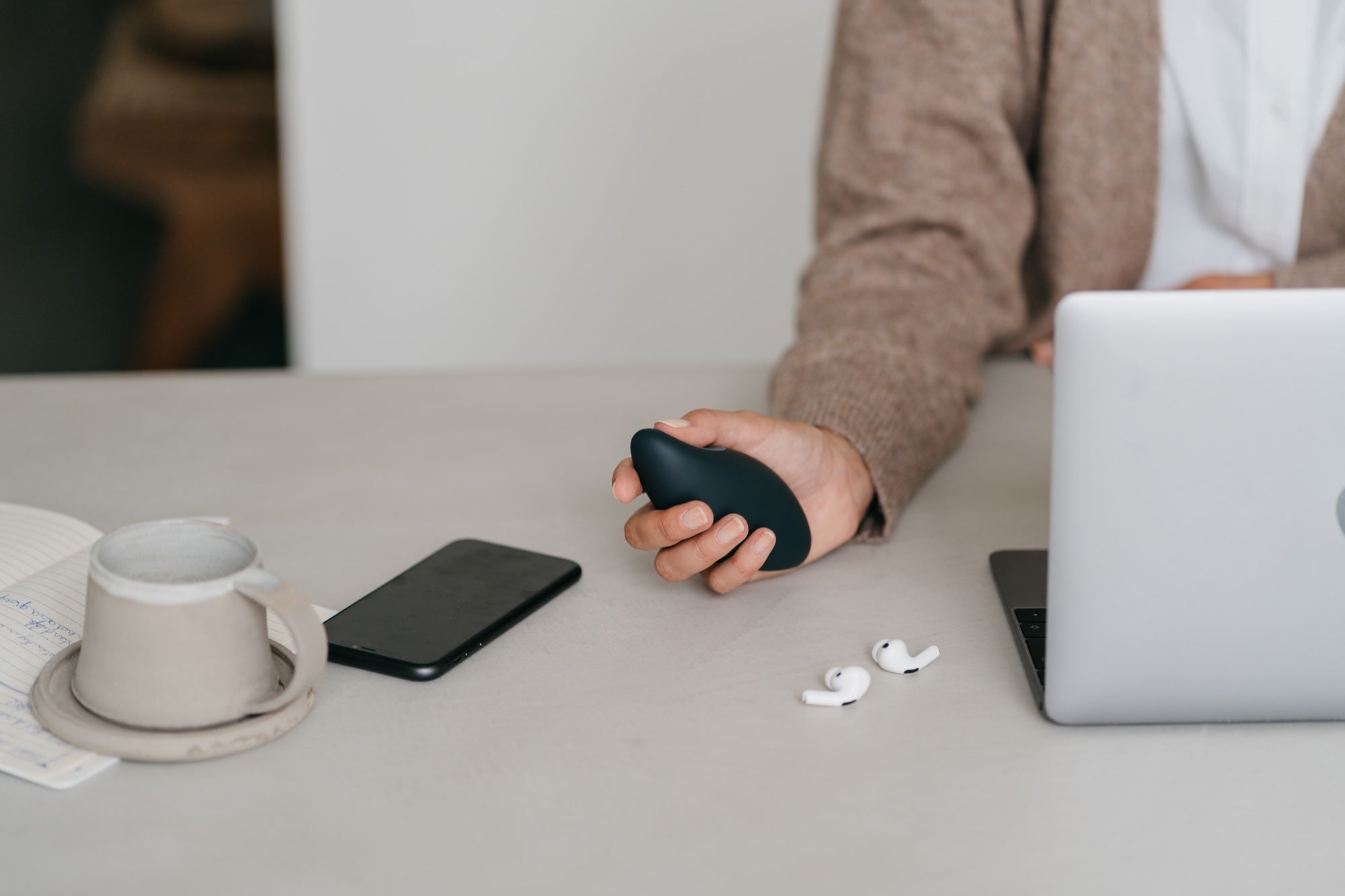 moonbird held at a desk beside a phone and laptop, with the thumb resting on its sensor